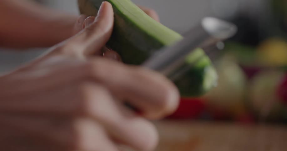 Person peels cucumber with metal peeler at counter