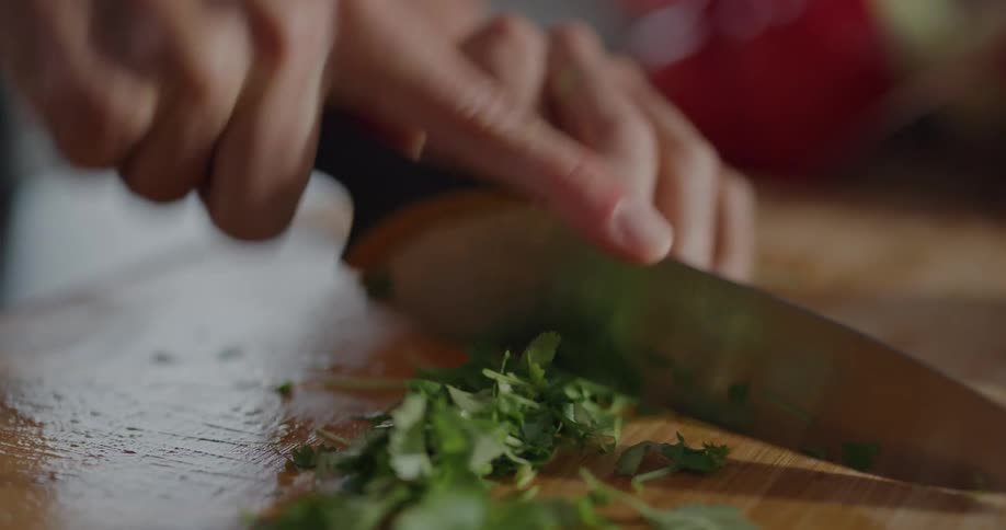 Person chopping cilantro on a cutting board with a knife