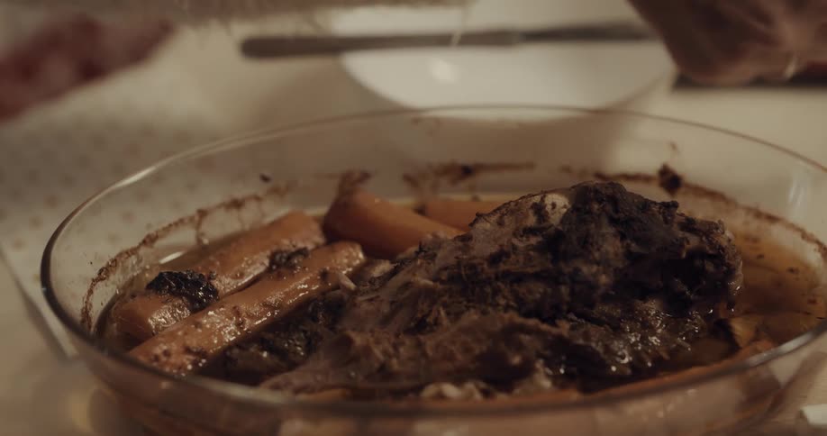A person passing a bowl of cooked carrots and roast while eating dinner at a table