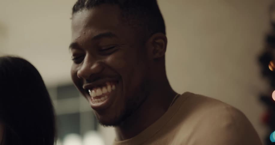 Man laughs next to woman in building in front of windows and christmas tree