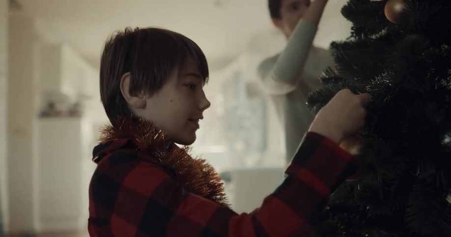 Teenage boy and his little brother decorates the tree for christmas in the living room at home