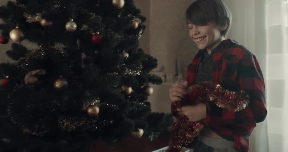 Two boys run to the christmas tree and open up boxes of decorations and start putting them on the tree