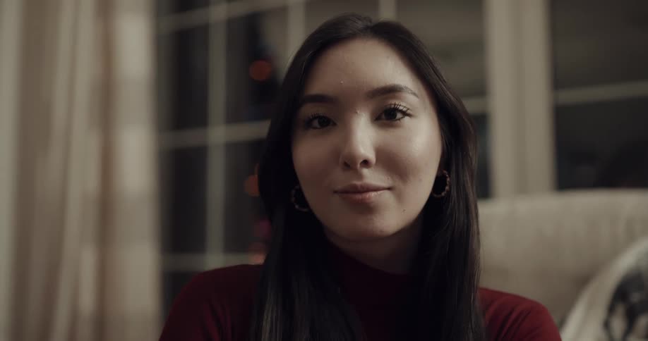 A young woman sitting in the living room of a house at night smiles into the camera