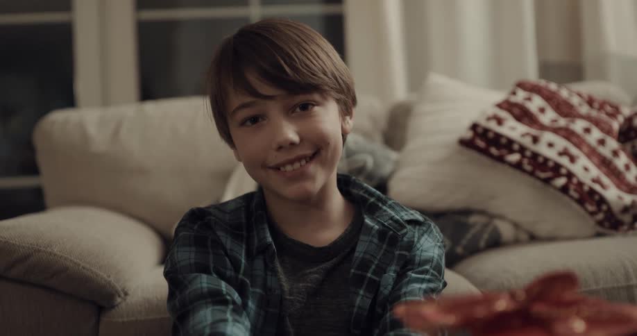Boy sitting in front of a sofa looks at the camera smilingly in the living room at home