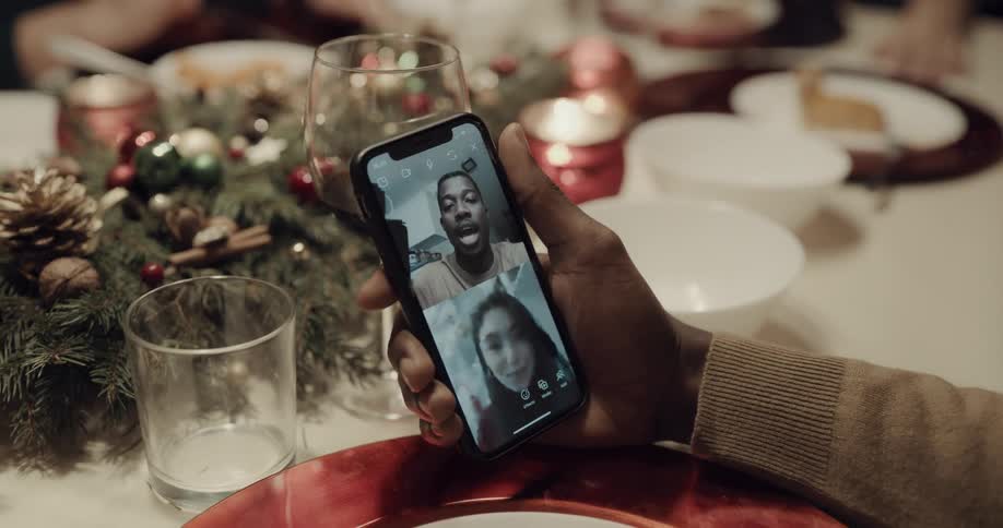 A man video chats on his cell phone while sitting at a dinner in a home