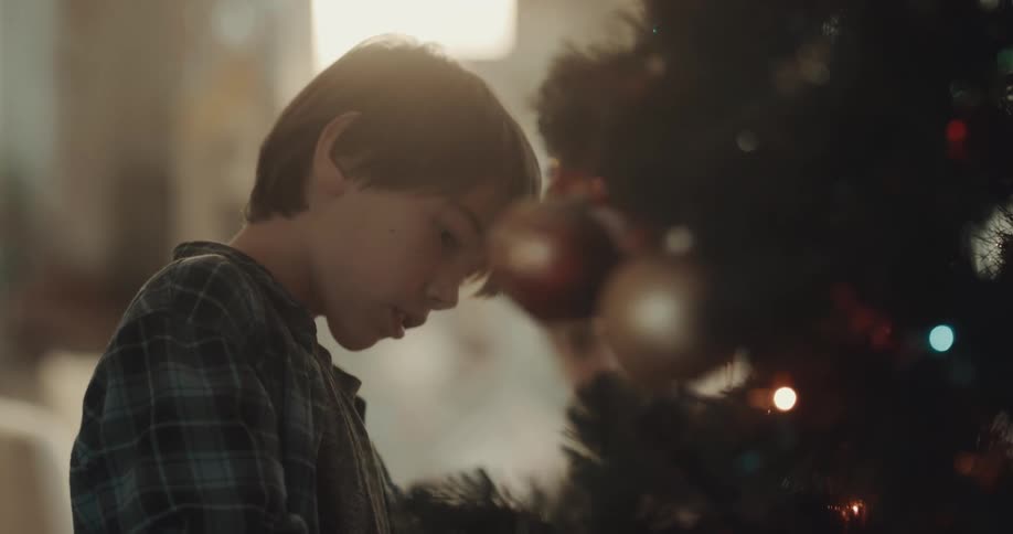 Boy decorates christmas tree talking and smiling
