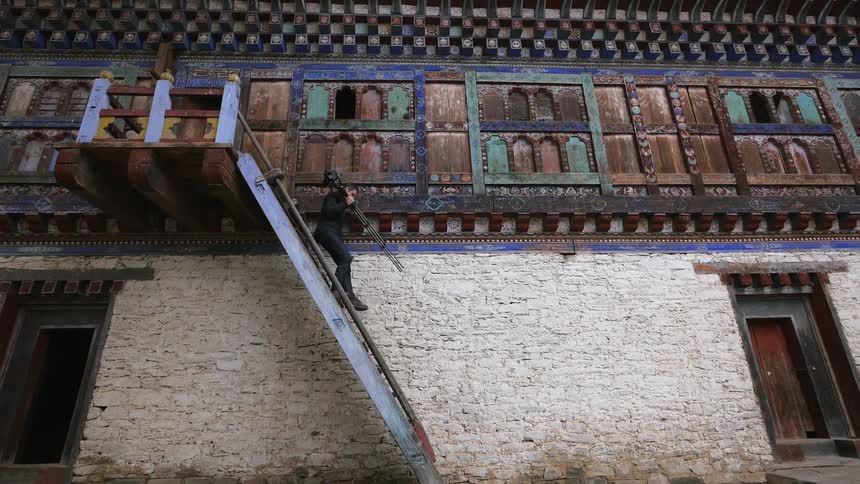 A man walking down steep stairs holding a camera with a tripod
