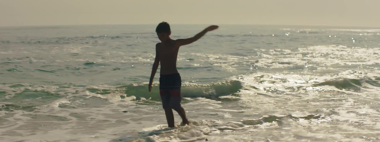 A young boy dances in the ocean waves coming to the shoreline
