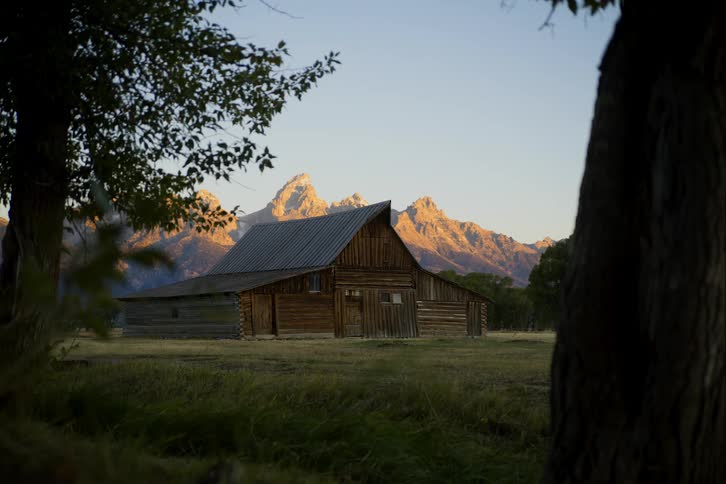 Time lapse of sunrise over an old barn sitting in field in front of mountain range