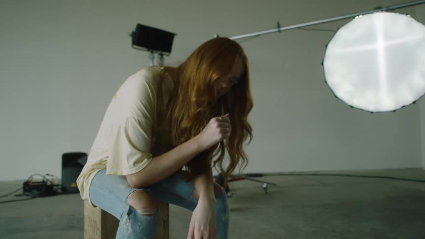 A caucasian woman sitting on a box in a photography studio posing for the camera