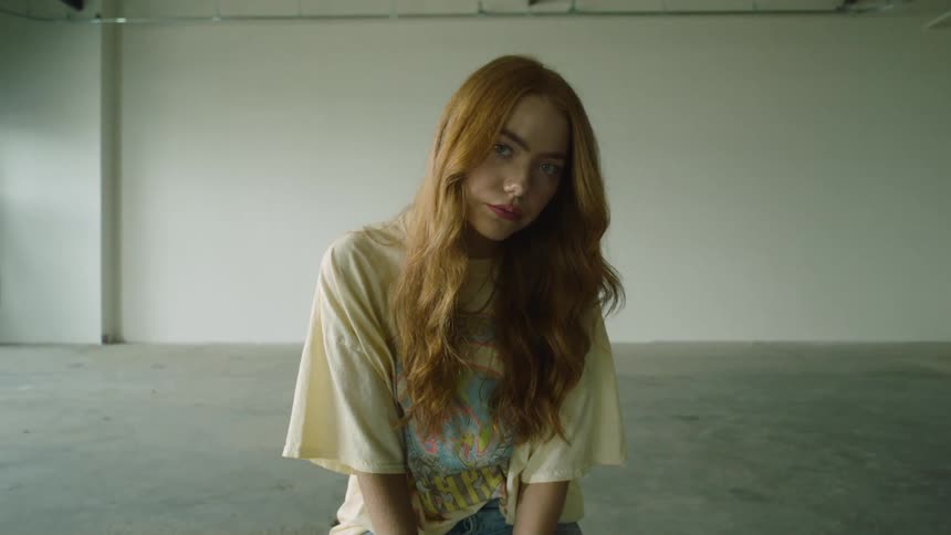 A woman sitting and staring in a room with a wall and a door in the background