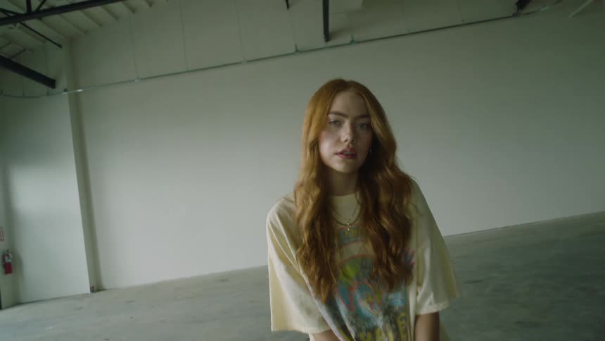 A young woman looks into the camera while sitting on a box in a large empty garage