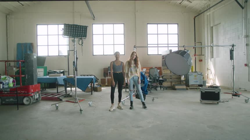 Two young women stand in a large garage with musician light and sound equipment