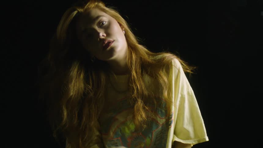 A young woman tilts her head and then raises her hand to pull back her long hair