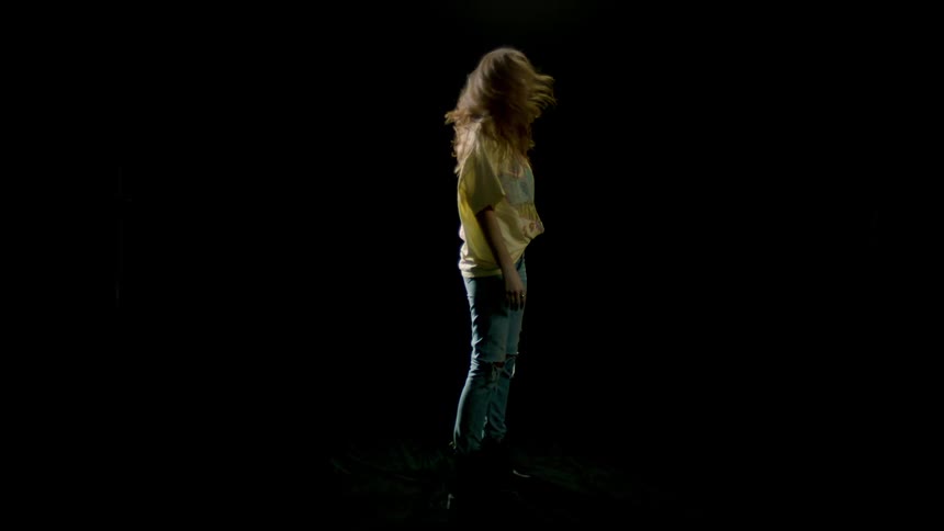 A young woman stands in place and spins in a dark studio