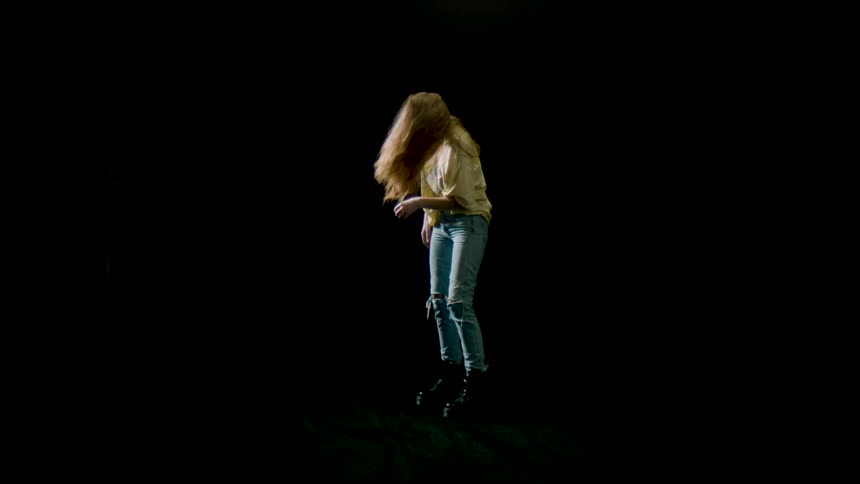 A woman with jeans and boots flicking her hair with a black background