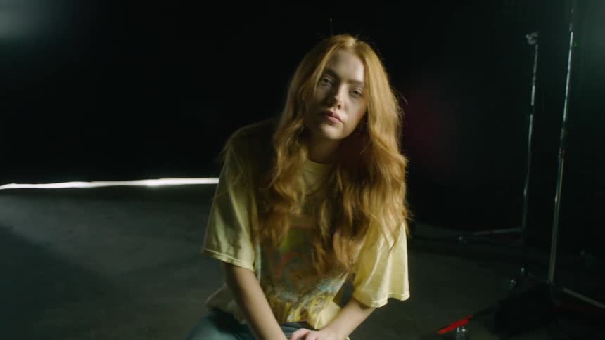 Woman with long hair sitting on a stool looking into the camera while swaying back and forth