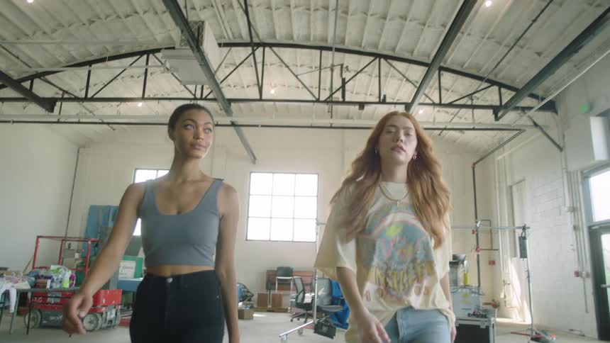 Two women are walking forwards inside a warehouse building on sunny day