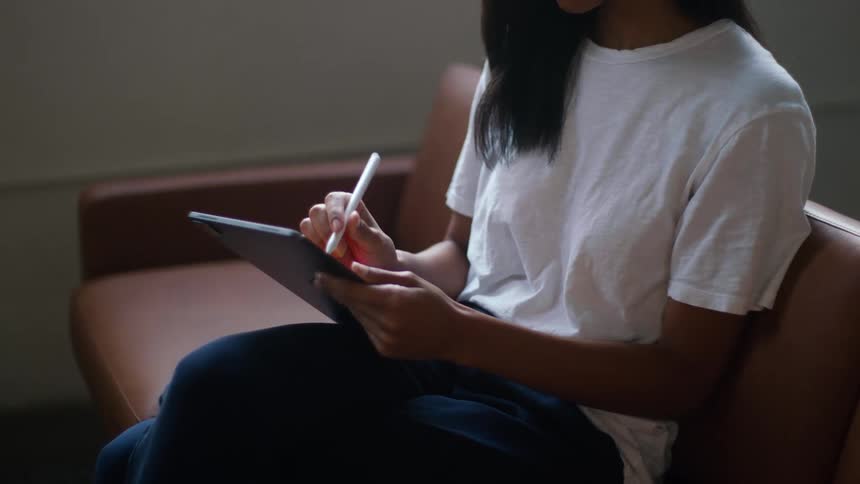 A woman sits on a couch at home and uses a tablet