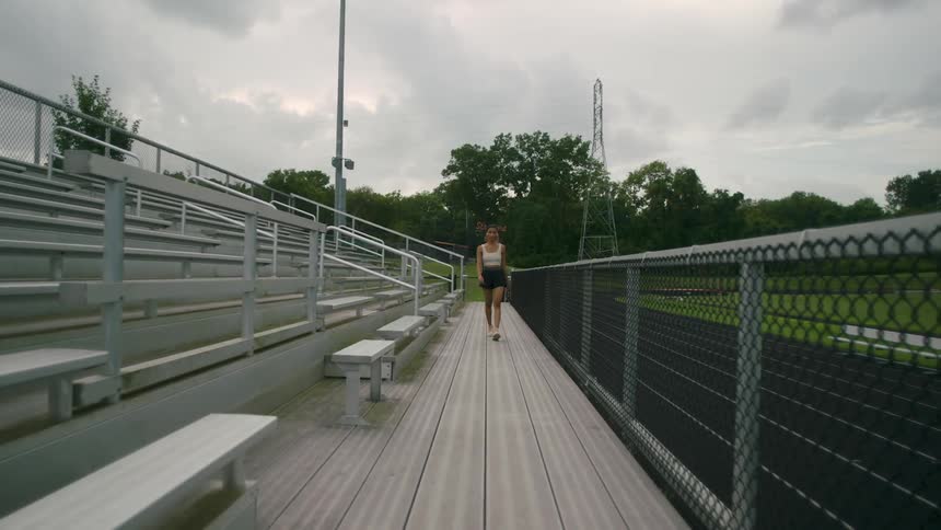 Woman wearing shorts walks between a fence and the bleachers