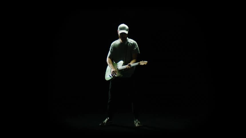 Man stands playing guitar indark room
