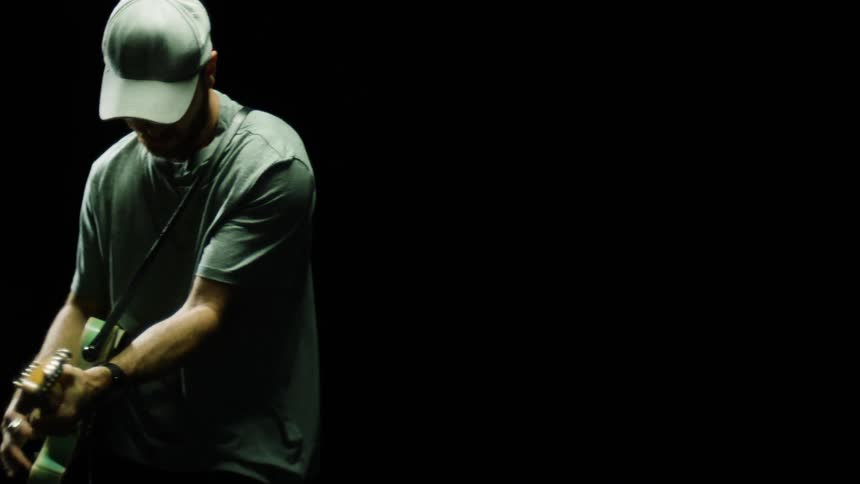 A man with a hat playing a guitar with a pick