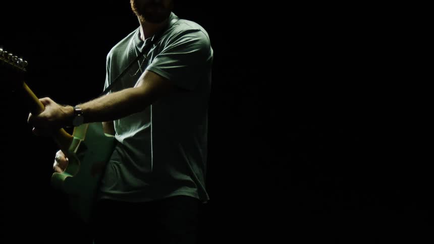 A man playing a guitar with a pick with a black background