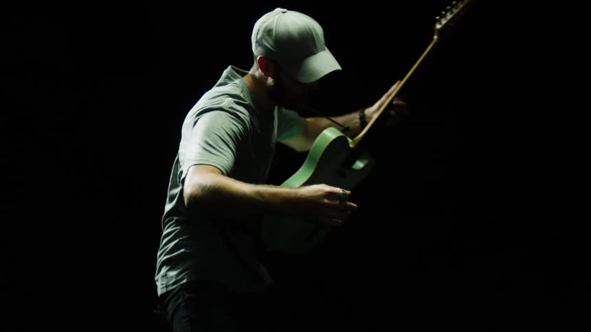 Man is swinging and playing a guitar in darkness