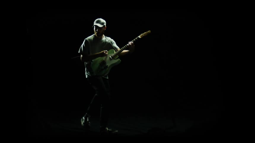 A man with a hat playing a guitar with a black background