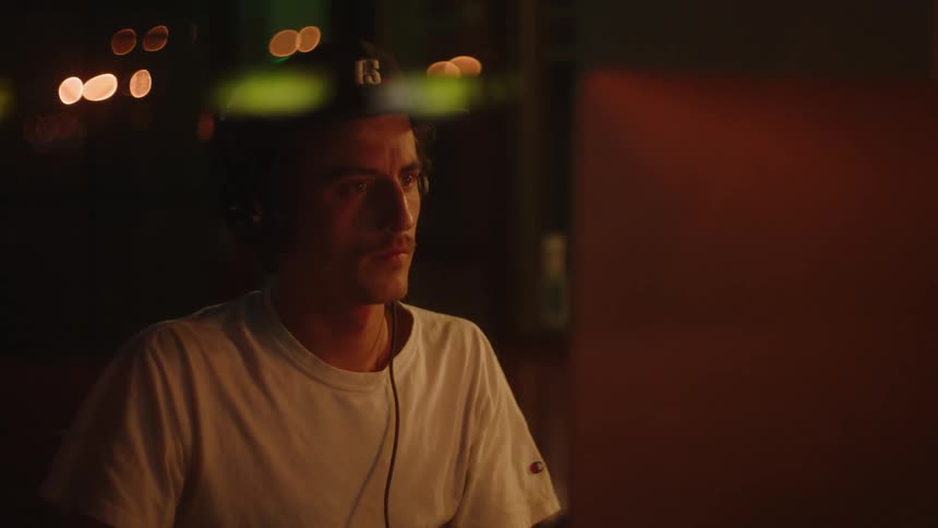 A man uses a computer at a desk in a dimly lit room at night