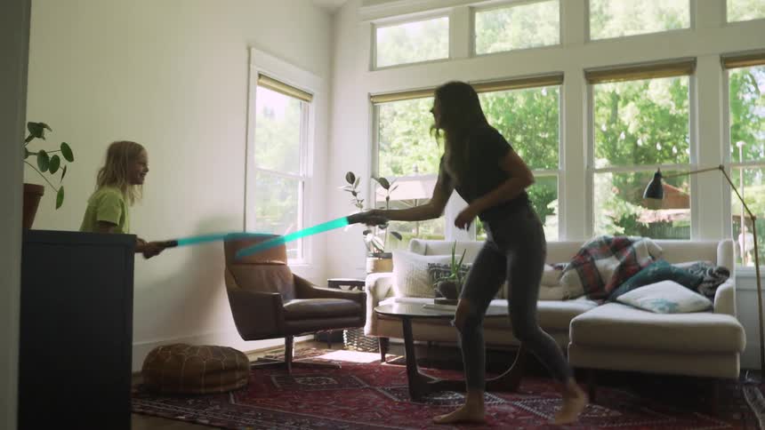 A mother and daughter play with toy light sabers in their living room