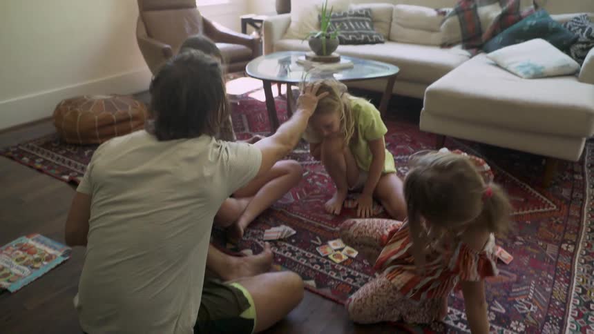 Father and daughters high five and play around on living room carpet