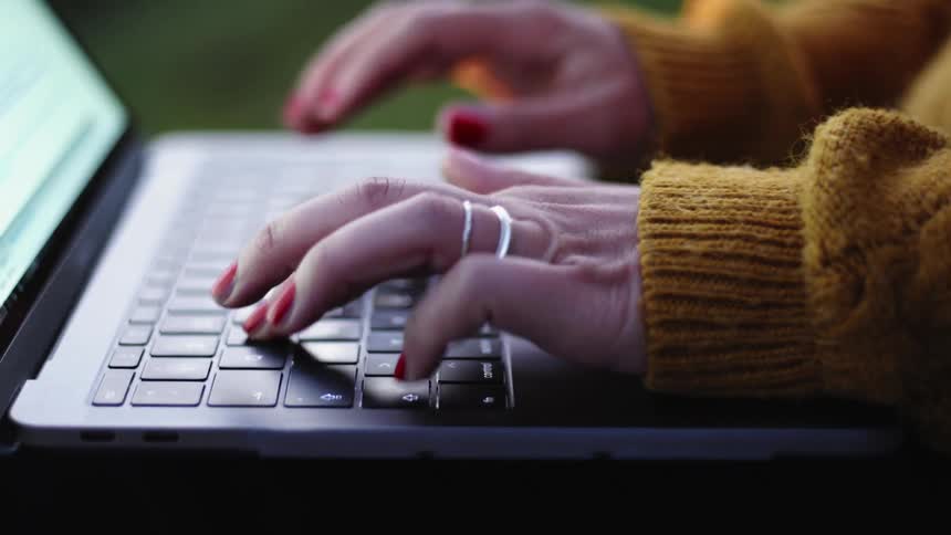Woman wearing ring types on laptop sitting in her lap