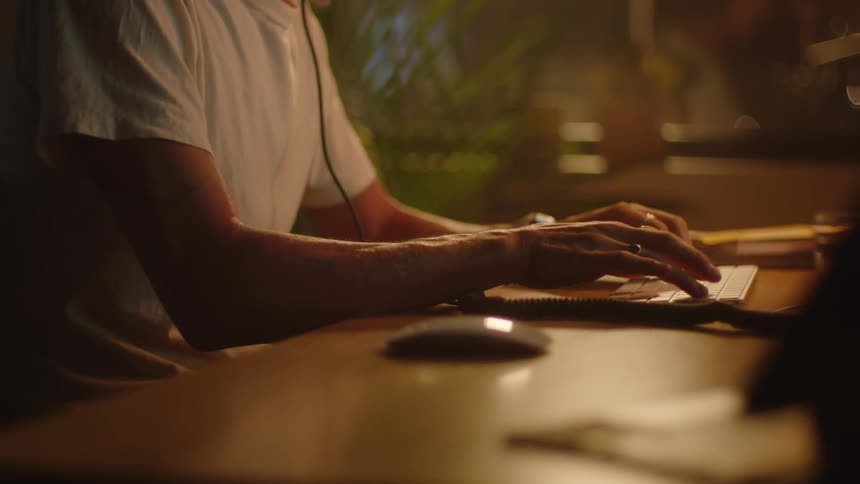 Person types on computer keyboard sitting at wooden table