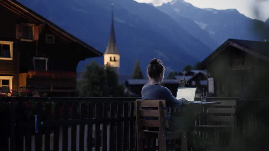 A young woman sits outdoors at a table as she works on her laptop