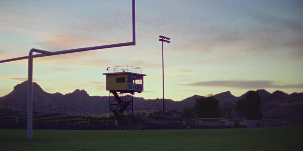 Tower with sports team name standing at the edge of a football field with a goal post and lights nearby