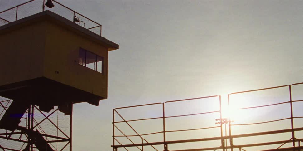 A press box next to hand railing with the sun the sky and clouds in the background
