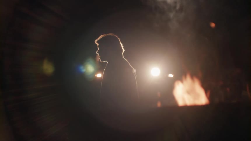 A man standing next to a fire throws his head back and laughs