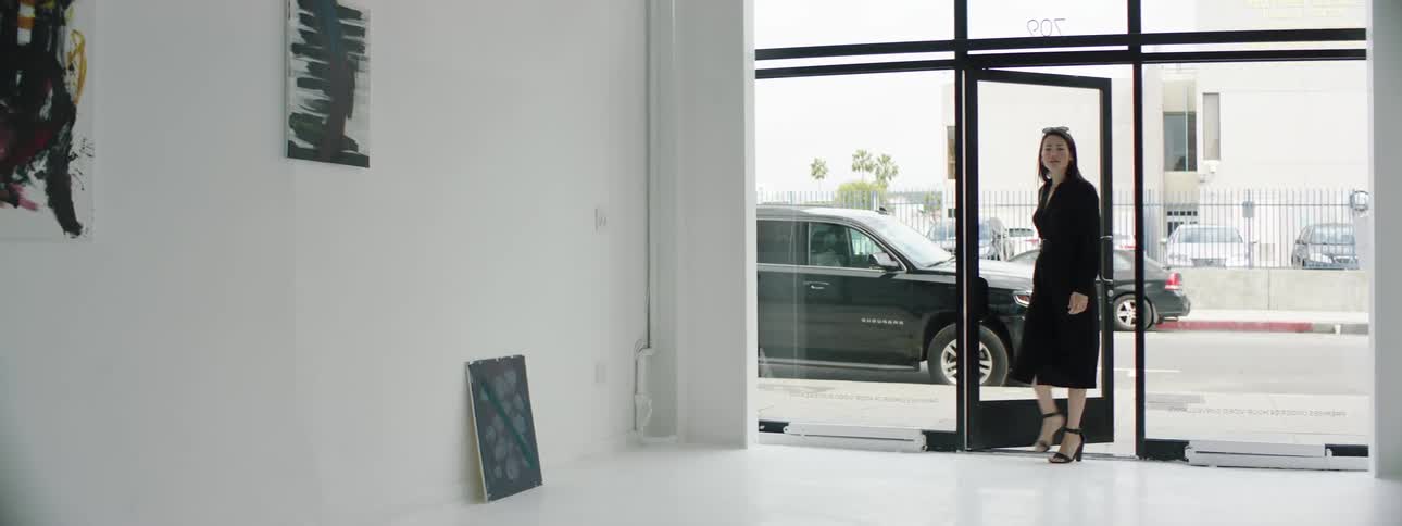 A woman with sunglasses opening a door and entering into a gallery with vehicles and a street in the background