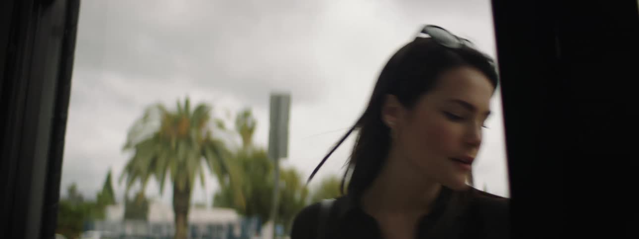 A woman with sunglasses entering into a store with vehicles a street the sky and clouds in the background