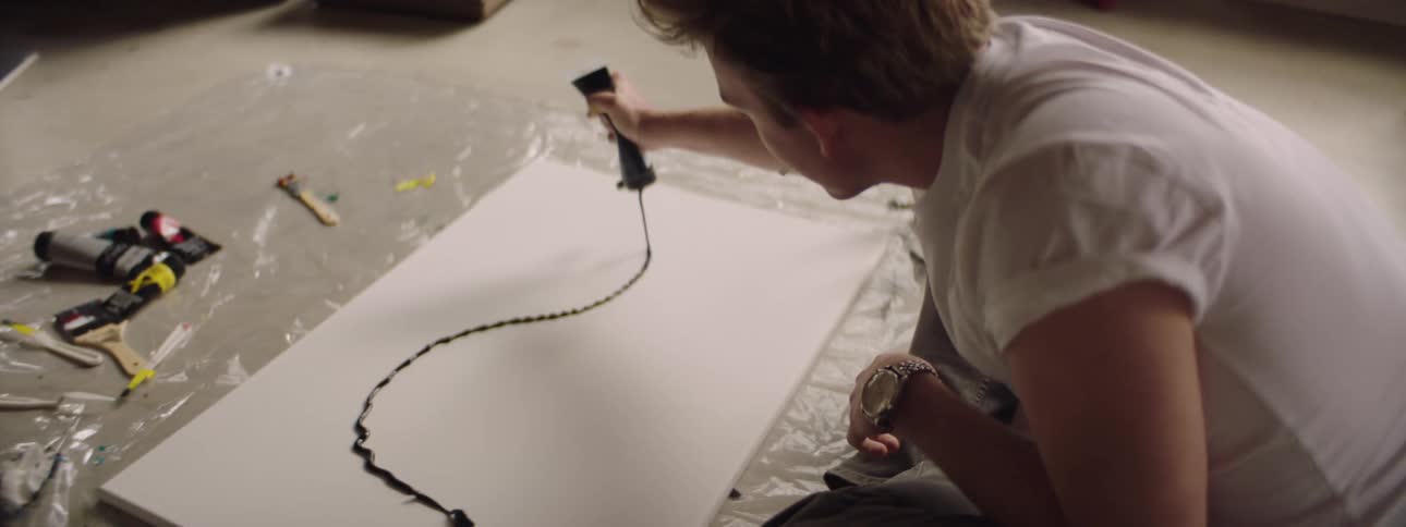 Man sitting on the floor of an art studio paints over canvas using ink