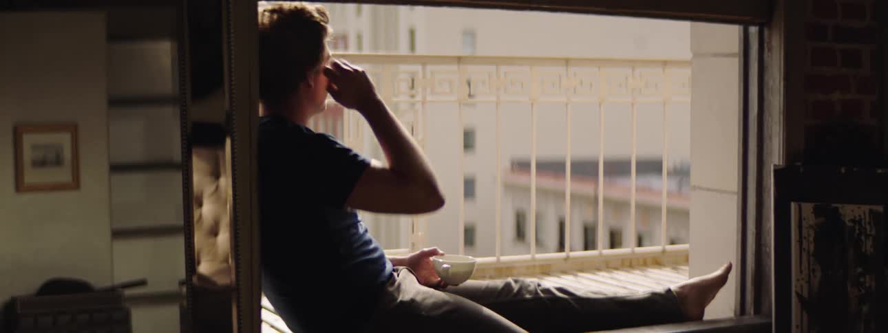 A man sitting in the window at home drinking a coffee