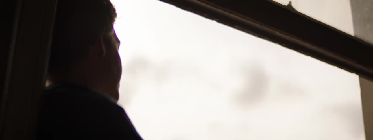 Silhouette of a young boy sitting in a window sill looking outside