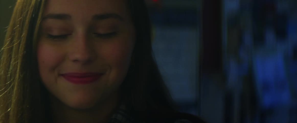 Young woman with makeup in a room glancing nervously at someone and smiling