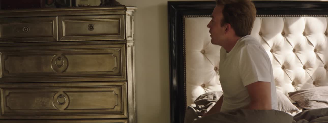 A man sleeping in bed awakens and retrieves his wristwatch from his dresser before walking out of the room