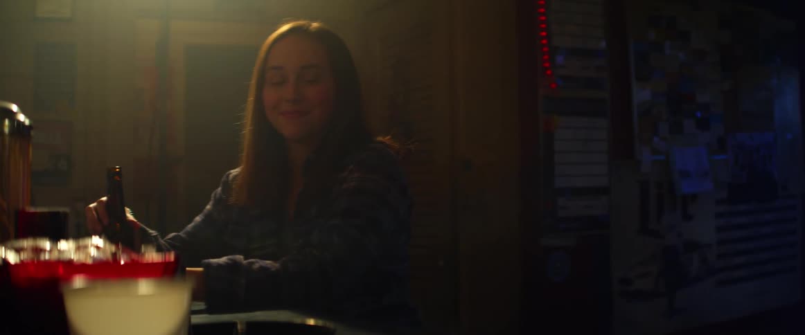 A woman smiles while sitting at a bar counter and holding a beer bottle