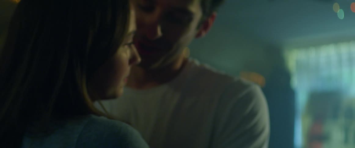 Man and woman dance close in a room with multicolored lights in front of a window where you can see a building