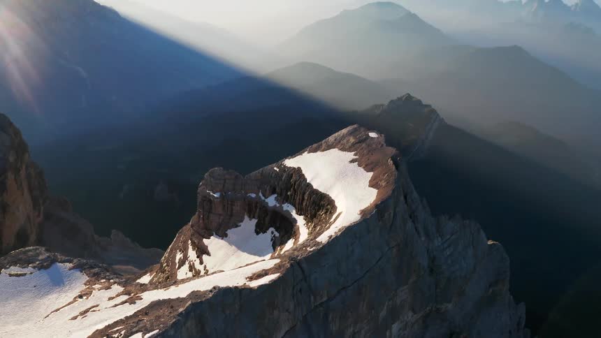Sun shines through fog over mountain range as snow covers plateau over cliff