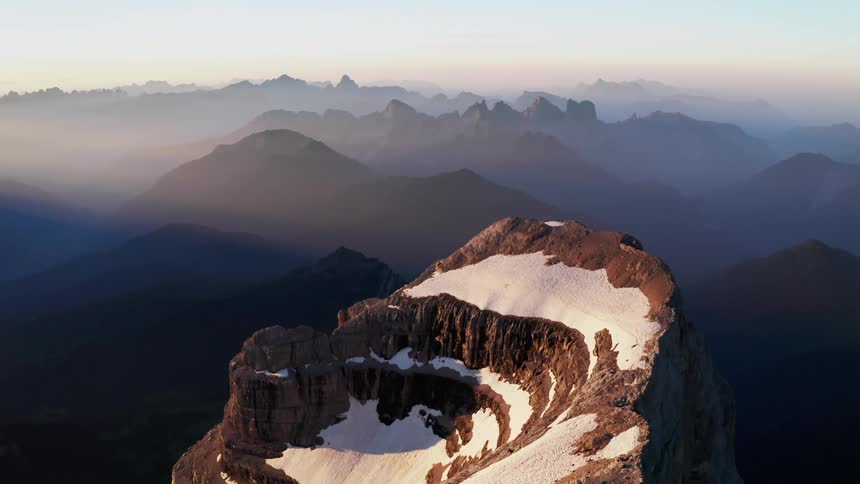 An aerial view of a snowy mountain peak in nature at sunrise