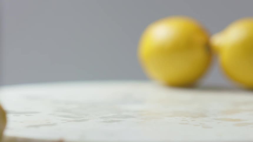 A person grabbing lemons that fell on a white surface with a gray background